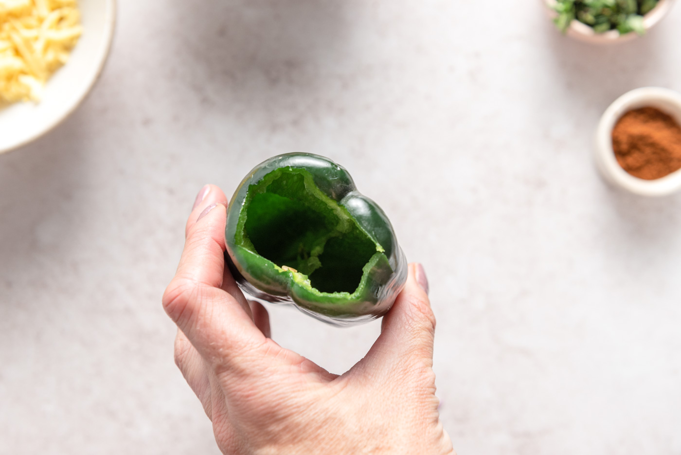 A hand holding a poblano pepper with the stem and seeds cut out from the top.