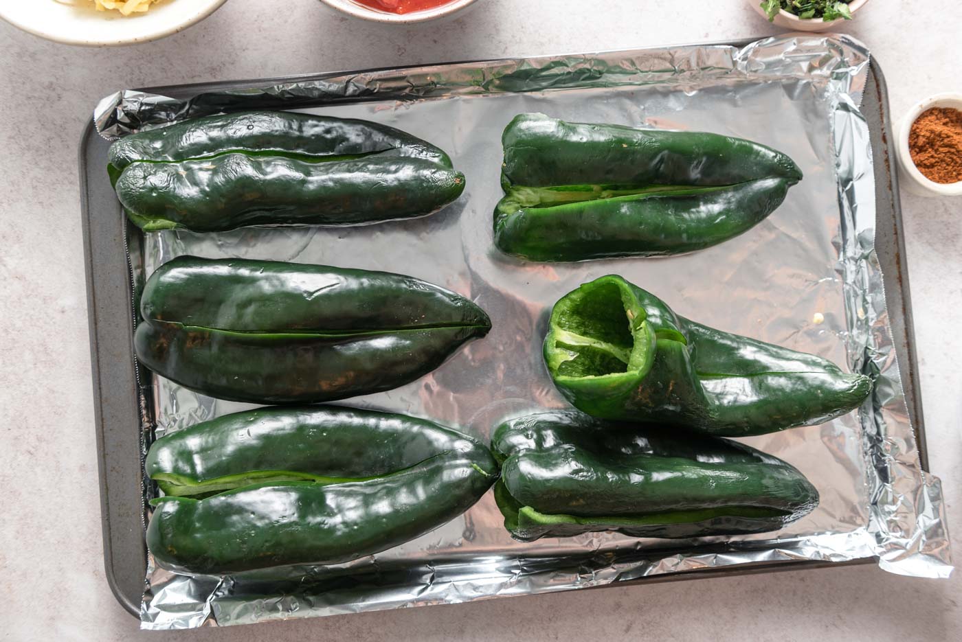 6 sliced open poblano peppers on a baking tray lined with foil.