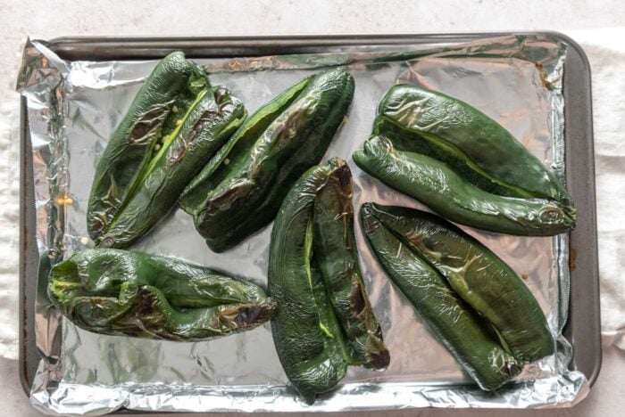 6 charred poblano peppers on a baking sheet.