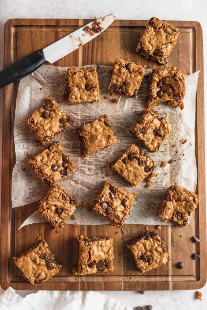 Vegan oatmeal chocolate chip cookie bars scattered on a wooden cutting board with a knife resting on the board.