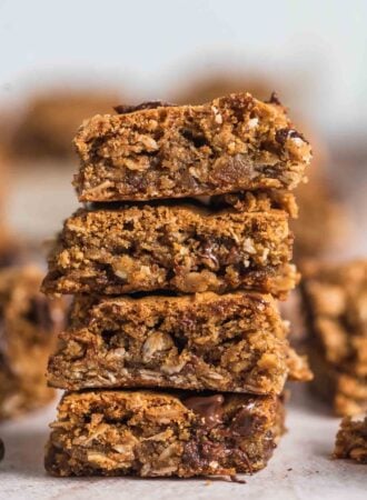 A stack of 4 vegan and gluten-free oatmeal cookie bars with chocolate chips in them. More bars can be seen in the background.