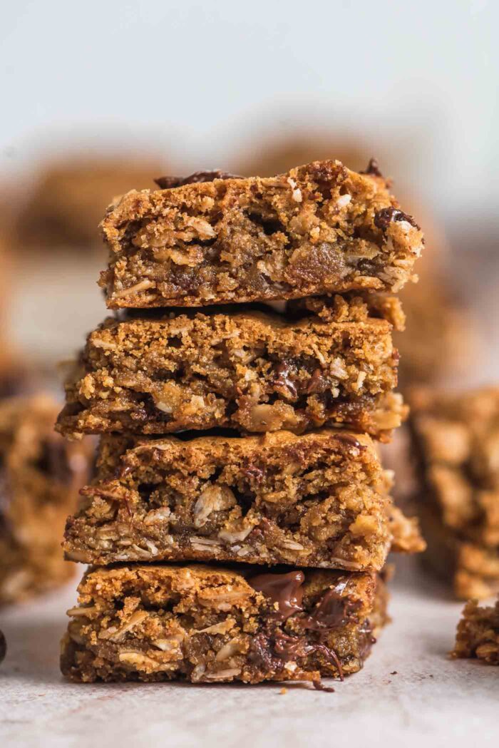 A stack of 4 vegan and gluten-free oatmeal cookie bars with chocolate chips in them. More bars can be seen in the background.