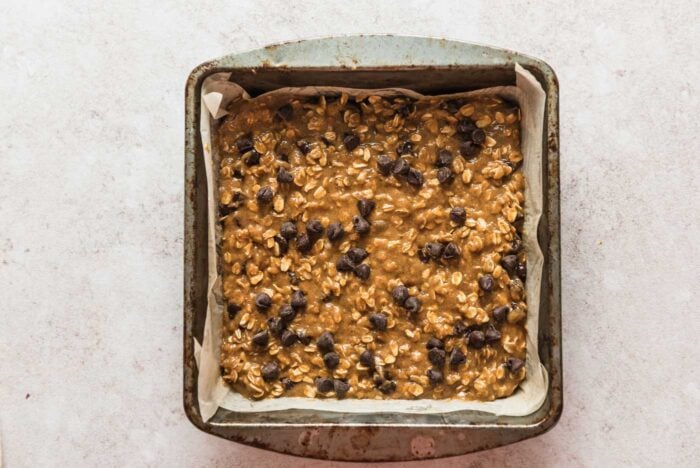 Raw chocolate chip oatmeal cookie bars batter in a baking dish lined with parchment paper.