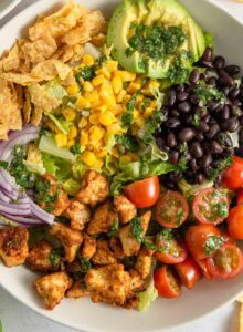 Overhead view into a santa fe salad with corn, avocado, black beans, tomato, tofu and red onion in a bowl.