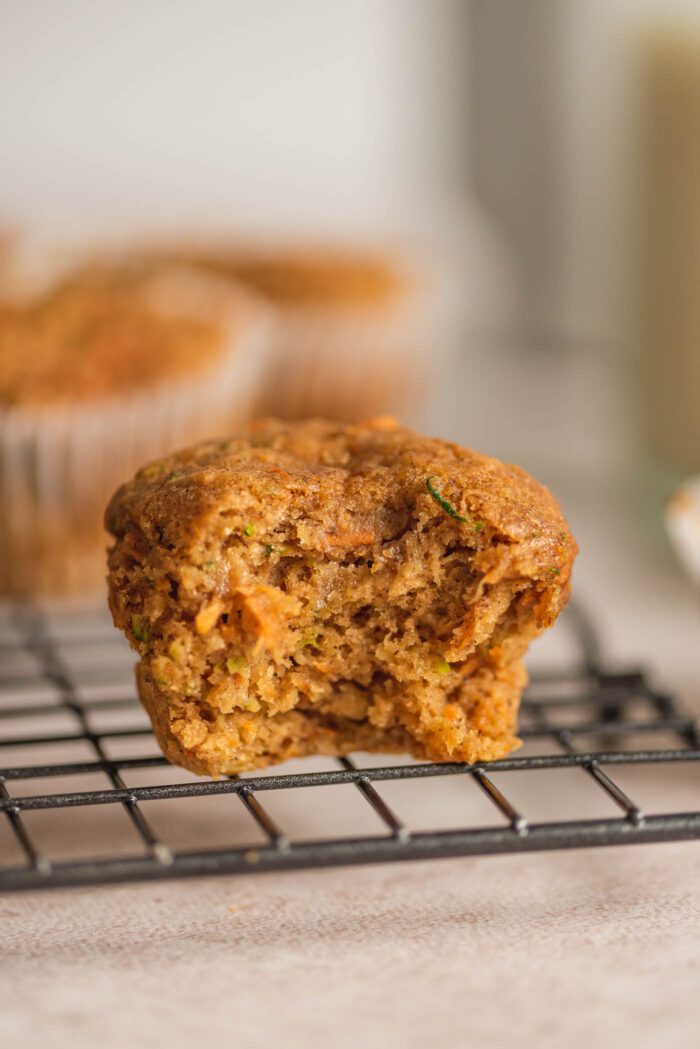 A carrot zucchini muffin with a bite from it on the edge of a baking rack.