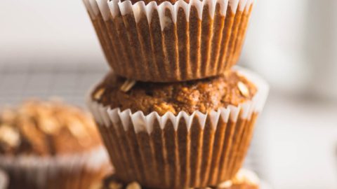 A stack of 3 oatmeal muffins in paper liners on the edge of a baking cooling rack.