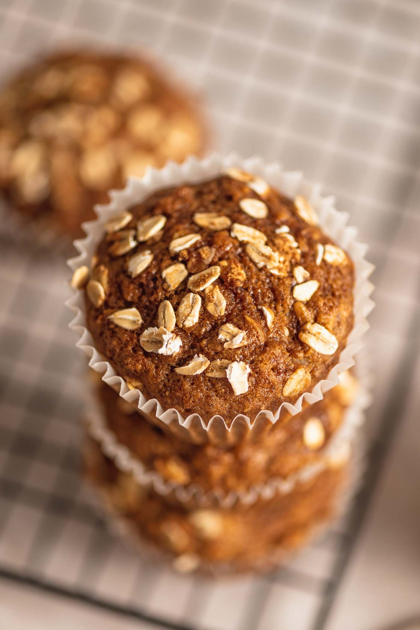 A stack of 3 oatmeal muffins in paper liners on the edge of a baking cooling rack.