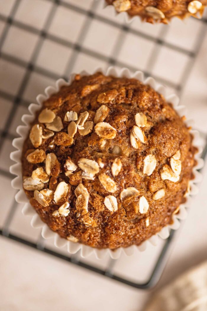 Overhead close up of a healthy oatmeal muffin topped with rolled oats and brown sugar sitting on a wire cooling rack.