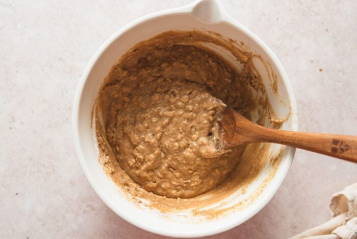 Raw oatmeal muffin batter in a mixing bowl with a wooden spoon resting in it.