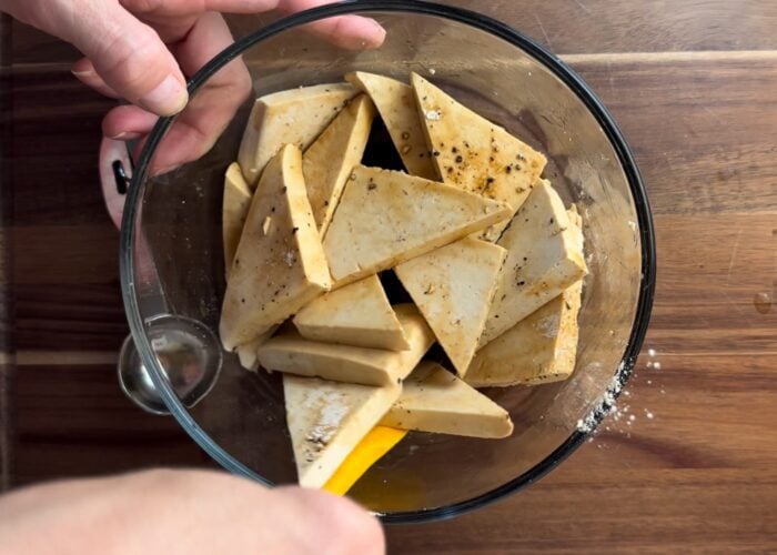 Tofu triangles being mixed in marinate in a container.
