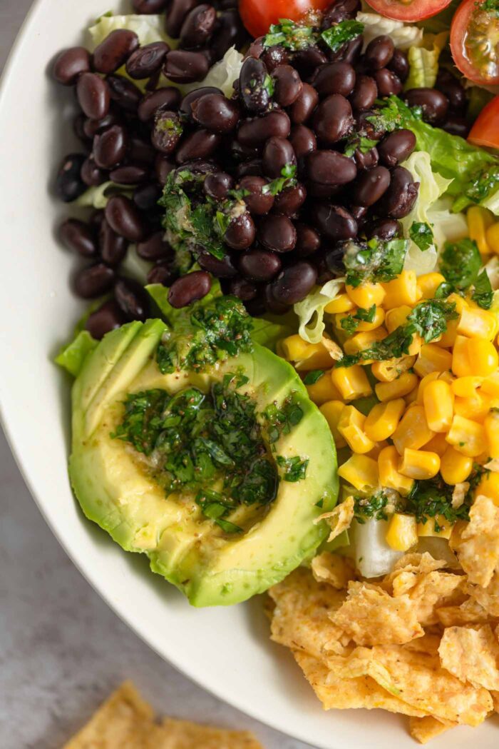 Close up of sliced avocado in a salad with black beans, chips, and corn topped with a cilantro dressing.