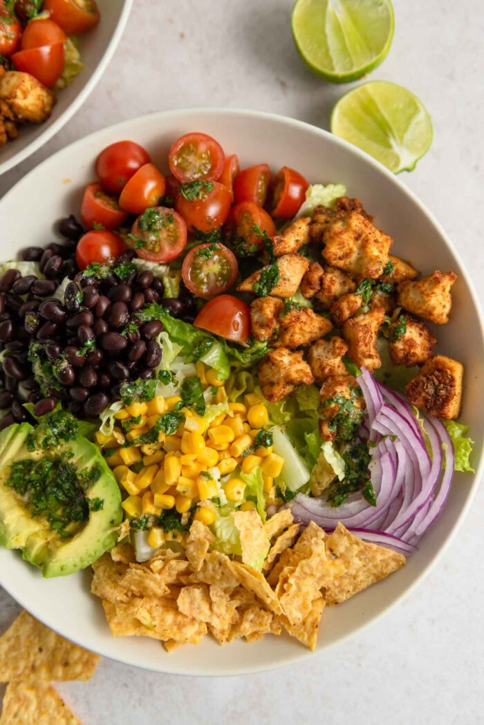 Overhead view of a santa fe salad in a bowl with corn, chips, red onion, black beans, tofu bits, tomato, avocado and lettuce.