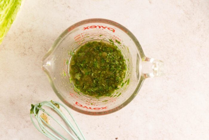 Cilantro lime vinaigrette in a measuring glass with a whisk beside it.
