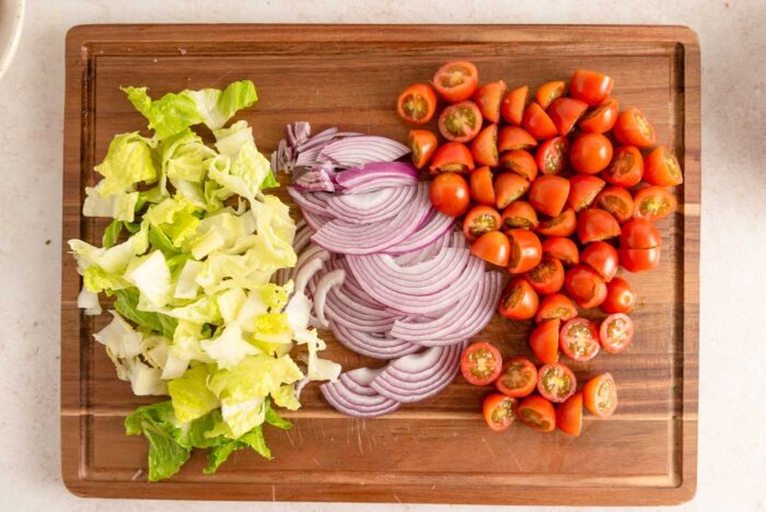 Chopped cherry tomatoes, romaine lettuce and red onion on a wooden cutting board.