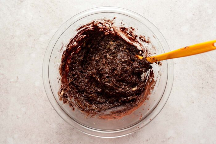 Thick zucchini brownie batter with chocolate chips mixed together in a mixing bowl with a spatula.