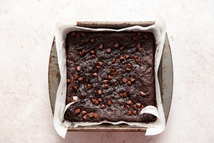 A baking pan of brownies sprinkled with chocolate chips. The pan is lined with parchment paper.