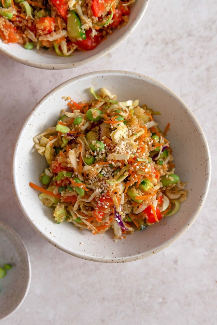 Overhead view of a bowl of quinoa salad with edamame, peppers, cabbage and green onion topped with sesame seeds.