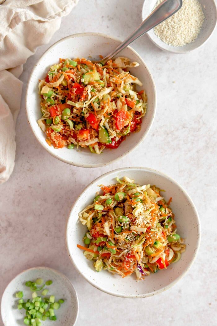 Two bowls of edamame quinoa salad with green onion, cabbage and carrot. There's a fork resting in one of the bowls.