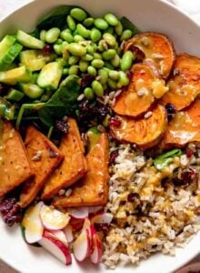 Overhead view of a vegetarian veggie power bowl with sweet potato, tofu, radish, cucumber, edamame and rice.