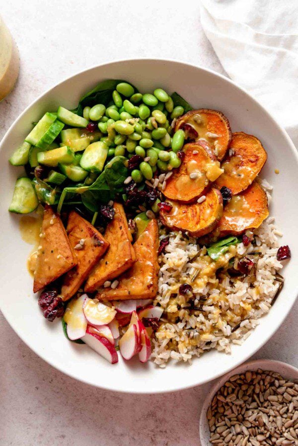 Overhead view of a vegetarian veggie power bowl with sweet potato, tofu, radish, cucumber, edamame and rice.