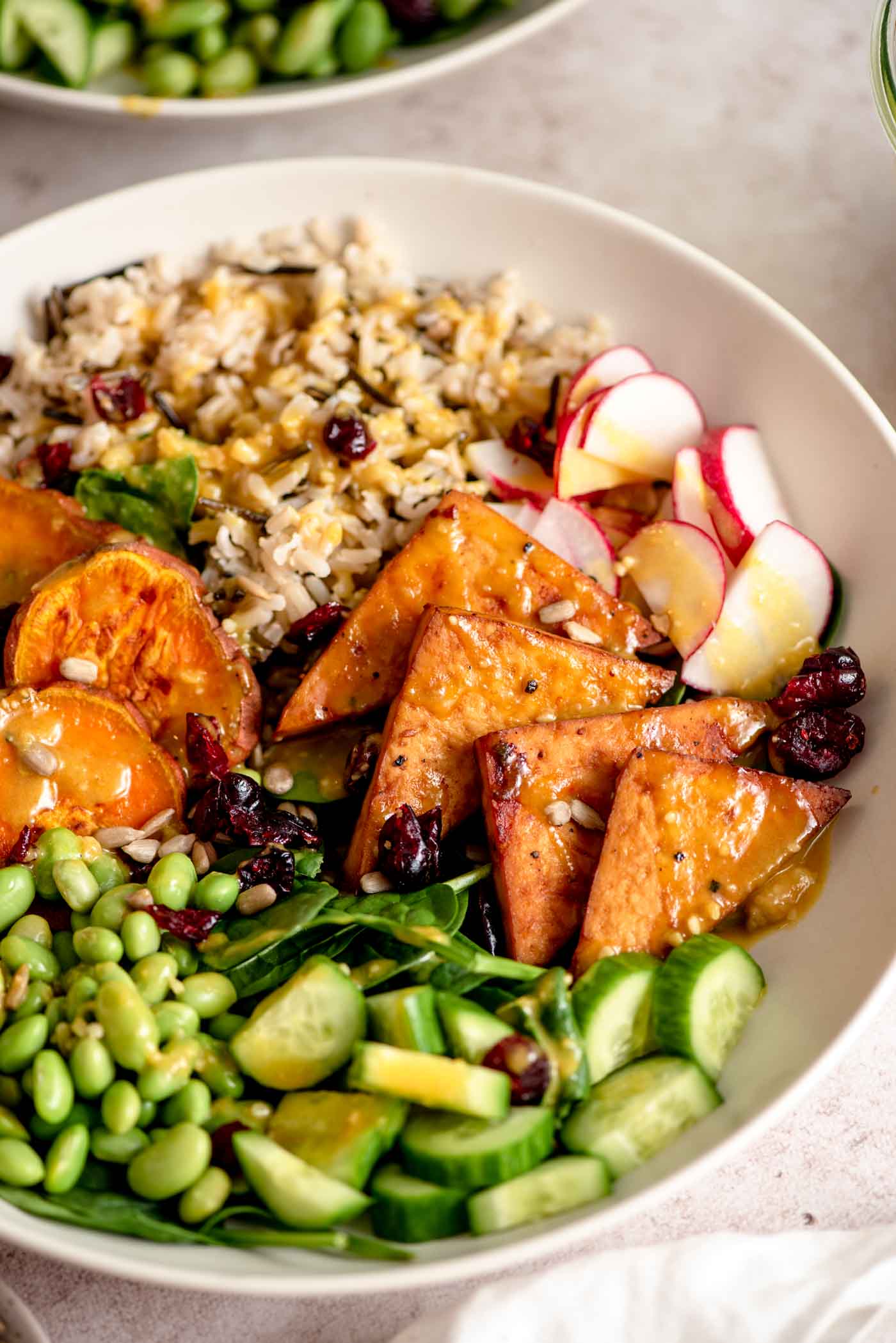 A colourful veggie power bowl with sweet potato, tofu, rice, edamame, cucumber, radish and spinach all topped with a creamy tahini sauce.