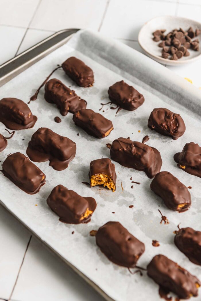 A baking sheet of homemade butterfinger candy bars. One bar has a bite out of it so you can see the texture inside.