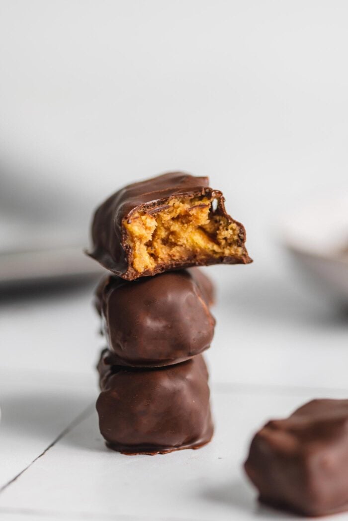 A stack of 3 mini homemade butterfinger candy bars. The one on top has been bitten into so you can see the peanut butter-corn flake filling.