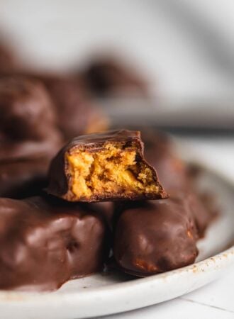 A plate of homemade butterfinger candy with one sitting on top with a bite out of it so you can see the crunchy texture inside.