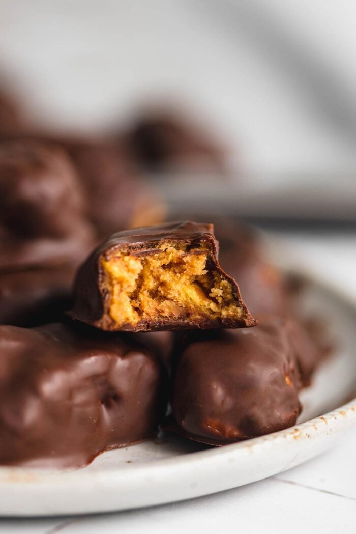 A plate of homemade butterfinger candy with one sitting on top with a bite out of it so you can see the crunchy texture inside.