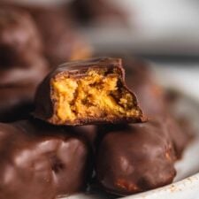 A plate of homemade butterfinger candy with one sitting on top with a bite out of it so you can see the crunchy texture inside.