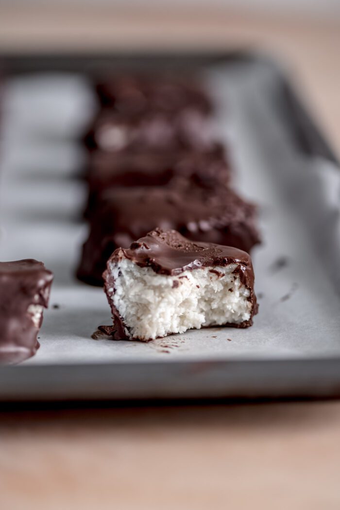 A homemade Mounds bar with a bite out of it so you can see the coconut filling inside the chocolate coating.