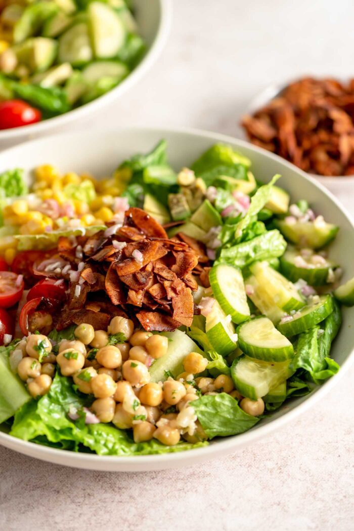 A bowl of vegan cobb salad with coconut bacon, chickpeas, corn, cucumber and tomato.