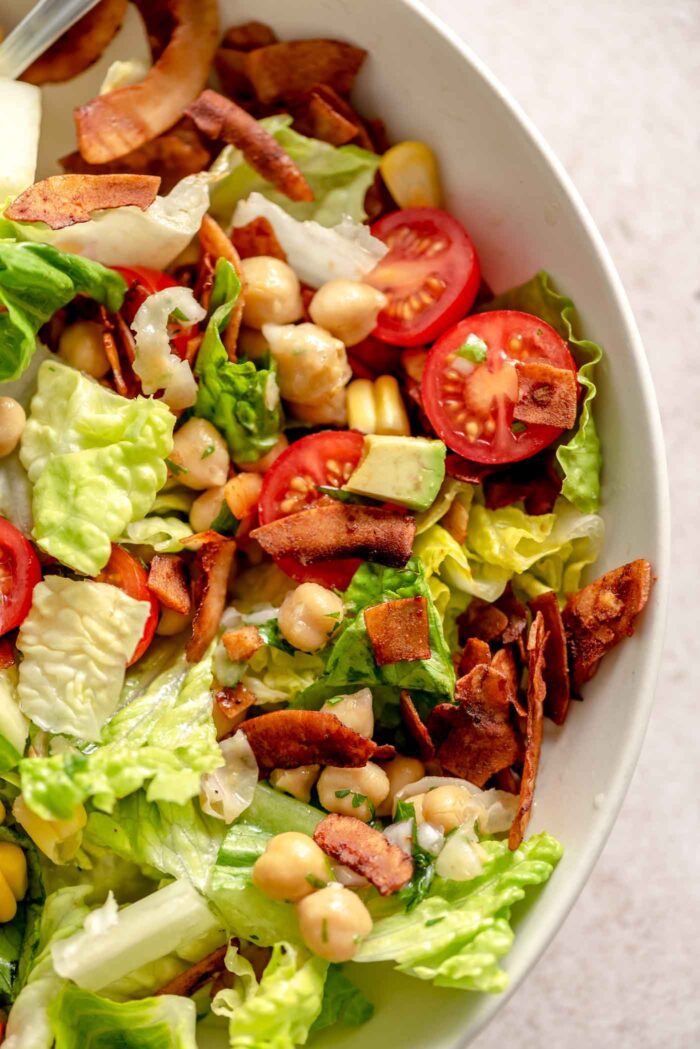 Mixed up vegan cobb salad with coconut bacon, tomato, chickpeas and lettuce in a bowl.
