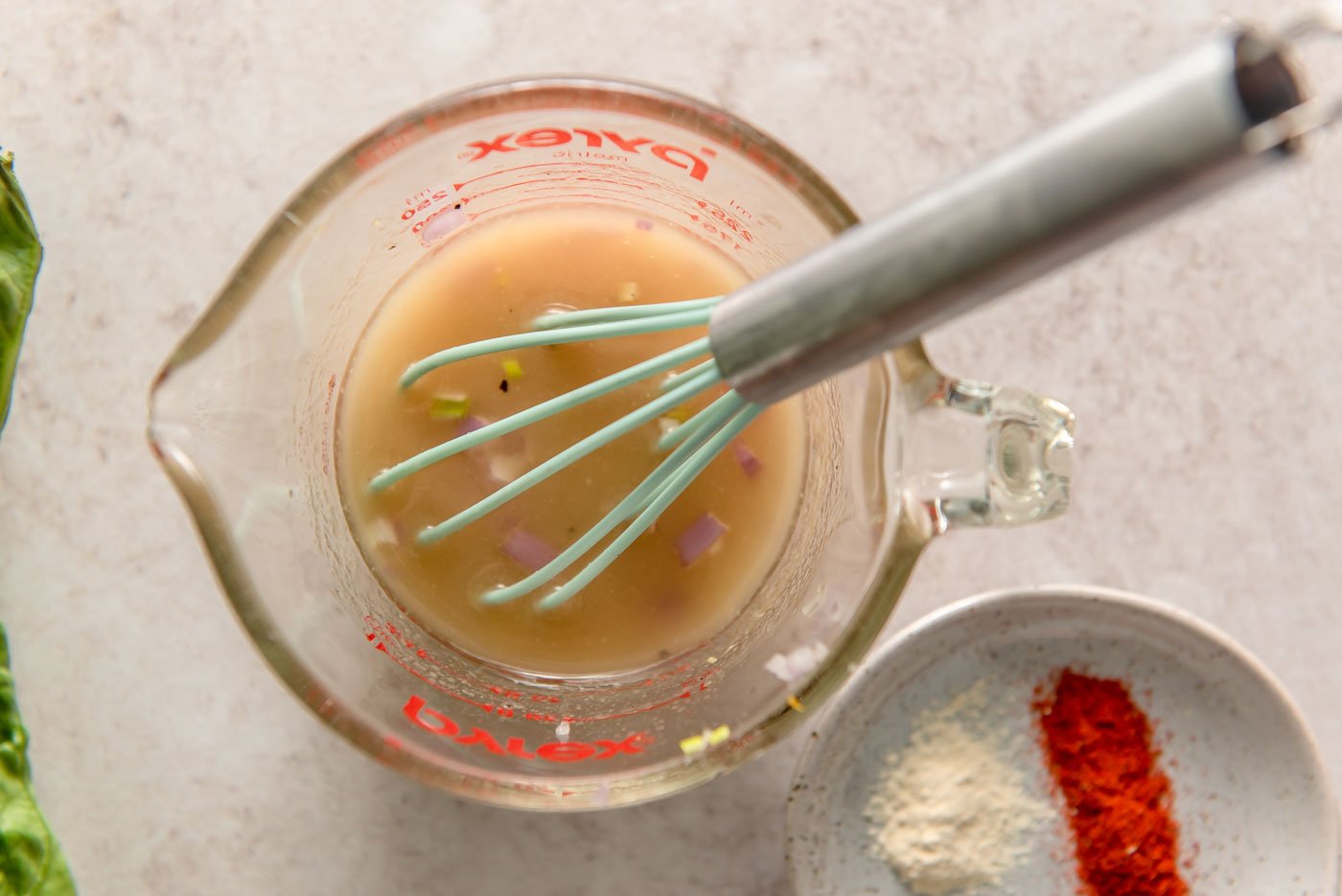 Italian vinaigrette with chopped shallot in a glass measuring up with a whisk resting in it.
