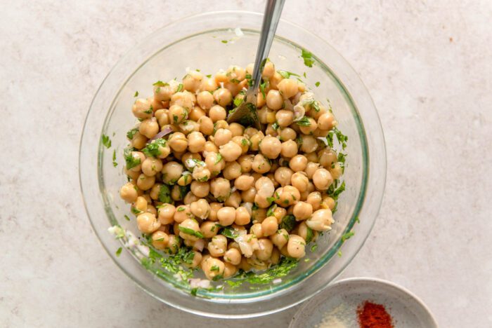 Chickpeas with chopped shallot and fresh herbs in a glass bowl with a spoon in it.