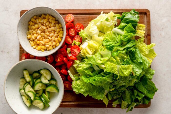 Chopped romaine lettuce, corn, cucumber and tomato on a cutting board.