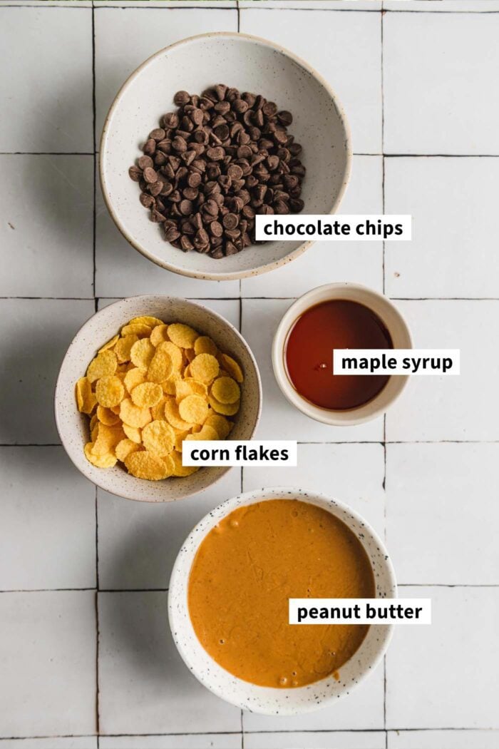 Chocolate chips, maple syrup, corn flakes and peanut butter each in a small dish and labelled with text overlay.