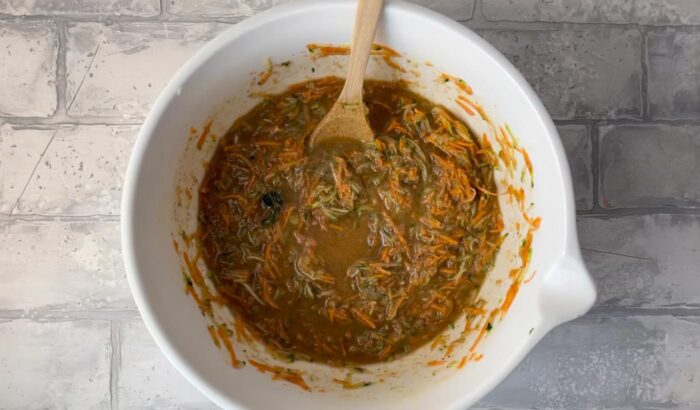Scrape carrot zucchini muffin batter into mixing bowl with a wooden spoon.