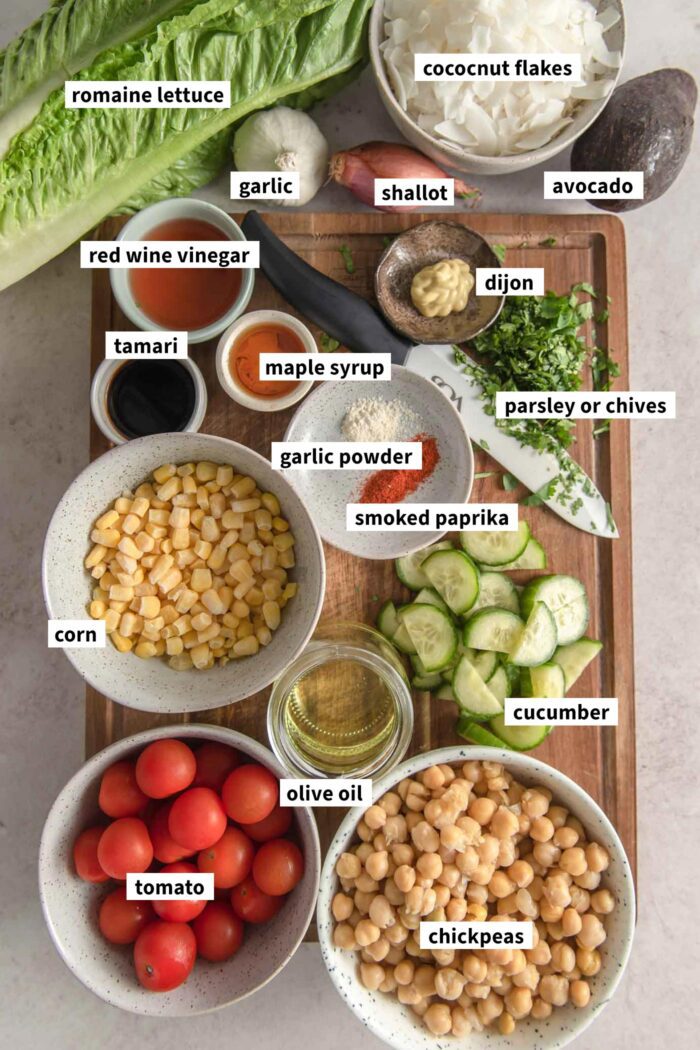 All of the ingredients for making a vegan cobb salad recipe with chickpeas and coconut bacon gathered in small bowls on a cutting board and labelled with text overlay.