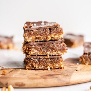 A stack of 3 chocolate caramel bars on a cutting board.