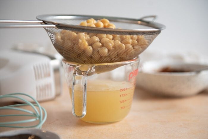 Chickpeas draining in a mesh seive over a measuring cup of aquafaba.