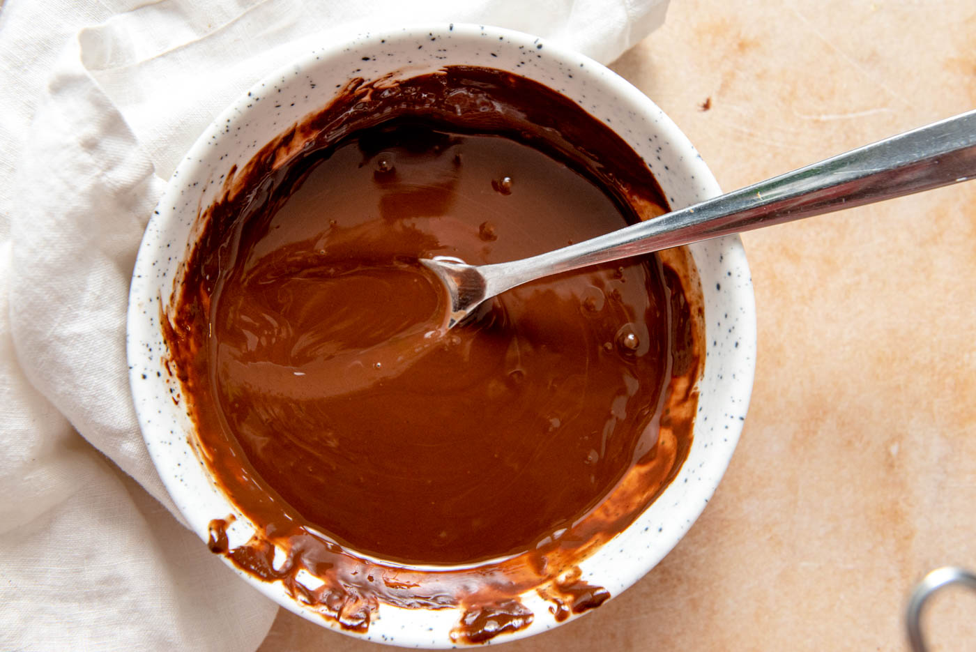 Small speckled dish of melted chocolate with a spoon resting in it.