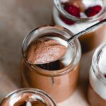 Spoonful of chocolate mousse resting on the edge of a small container of chocolate mousse with 3 more containers placed around it.