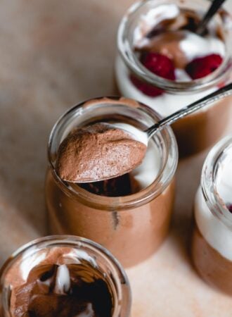 Spoonful of chocolate mousse resting on the edge of a small container of chocolate mousse with 3 more containers placed around it.