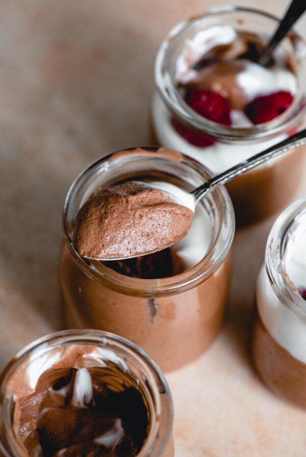 Spoonful of chocolate mousse resting on the edge of a small container of chocolate mousse with 3 more containers placed around it.