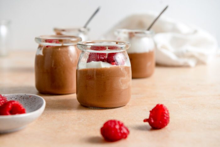 3 small containers of chocolate mousse topped with whipped cream and raspberries.