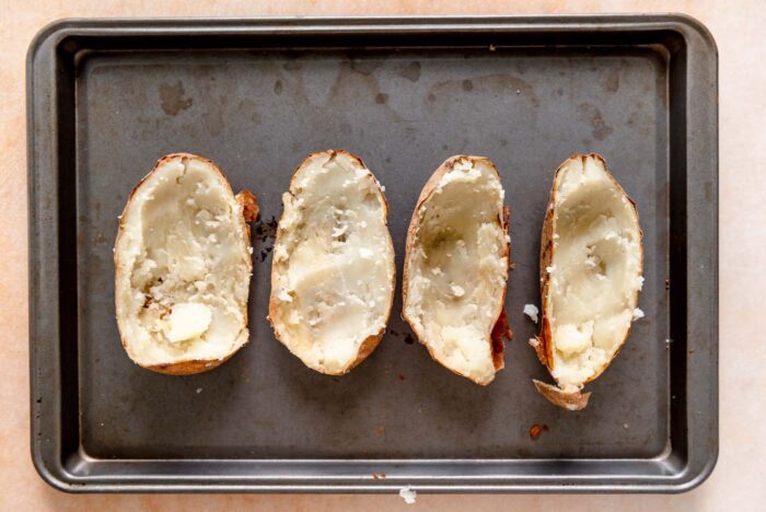 4 potato skins with the potato flesh scooped out on a baking sheet.