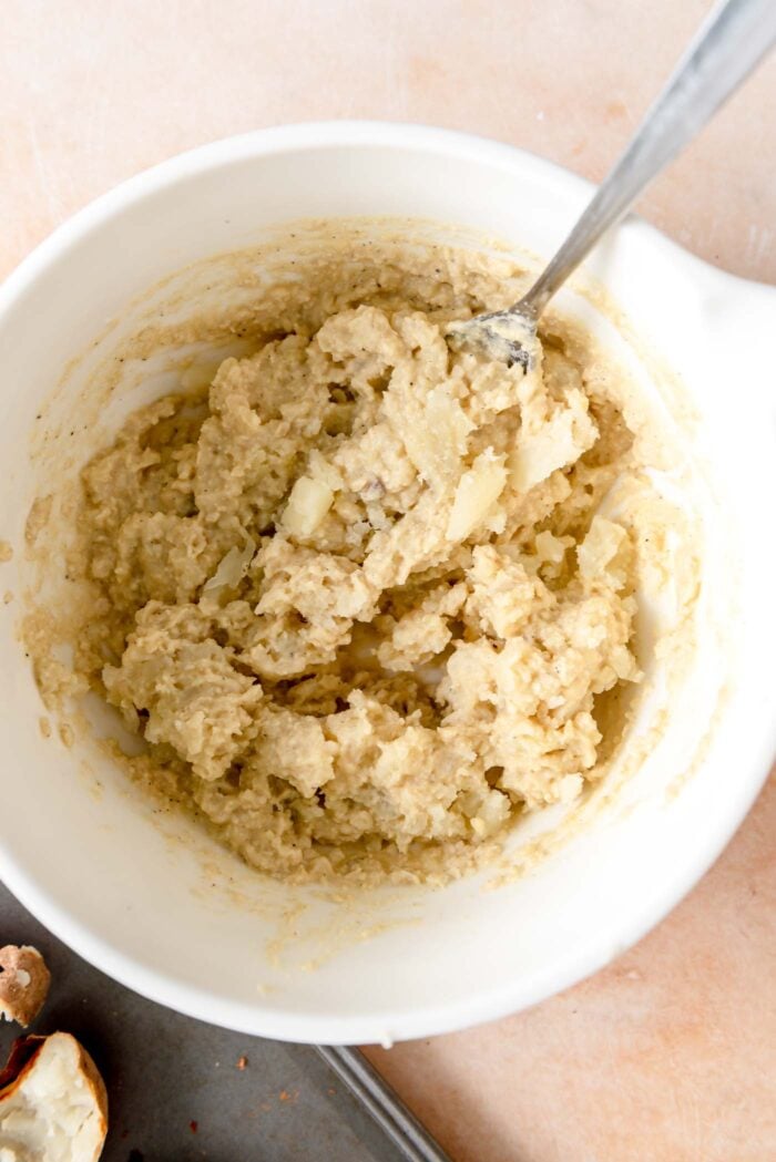 Mashed potato mixed with cashew cream in a mixing bowl with a spoon resting in it.