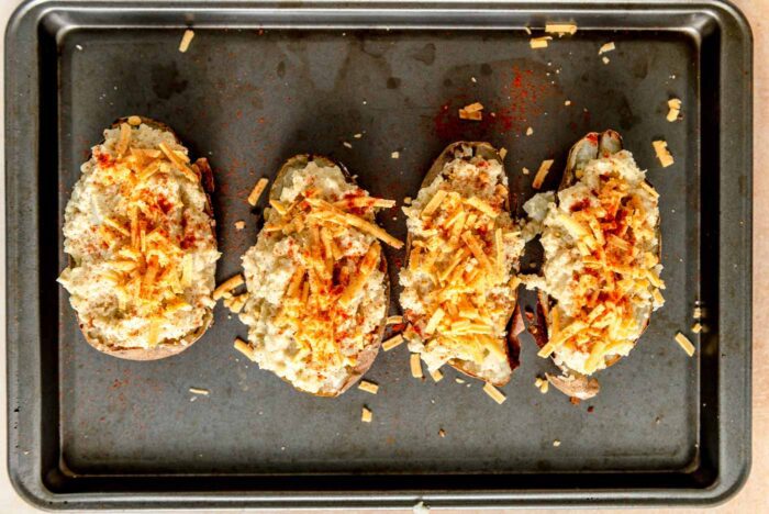 Four twice baked potatoes topped with cheese on a baking sheet.