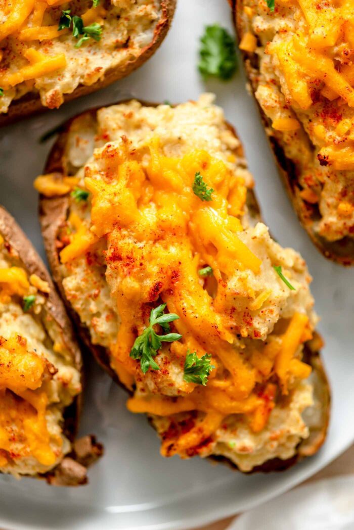 Twice baked potatoes topped with melted cheddar cheese and paprika on a baking sheet.
